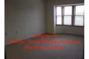 Empty living room with beige carpet, white walls, and a large window with mini blinds allowing natural light to enter.