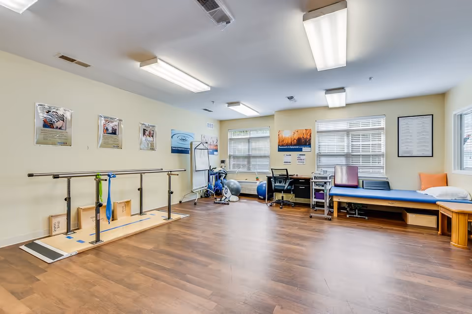 Bright physical therapy room with parallel bars, exercise equipment, therapy tables and desks.