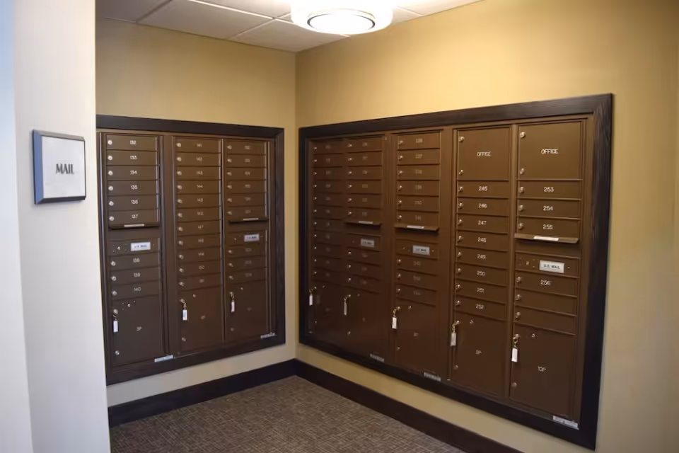 Wall-mounted community mailboxes in a small interior mail room with a 'MAIL' sign on the wall.