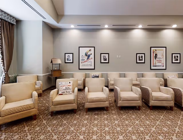 Rows of beige armchairs arranged in a communal lounge with framed posters on the wall and patterned carpet.