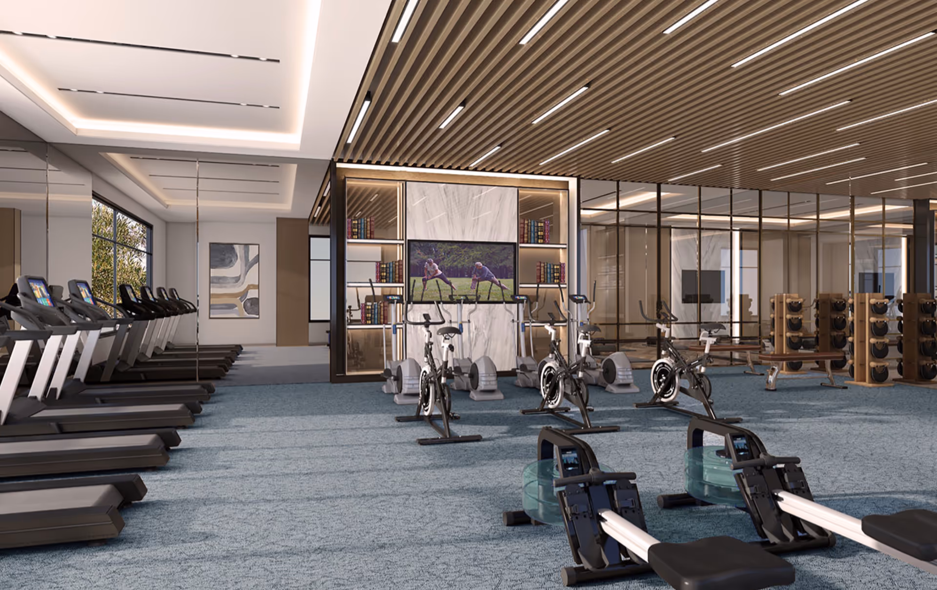 A modern fitness center with multiple treadmills lined up on the left, stationary bikes in the center, and rowing machines in the foreground. The room features a blue carpet, a wooden slatted ceiling with recessed lighting, and a large TV mounted on a marble wall with bookshelves on either side. There are also weight racks and benches visible in the background.
