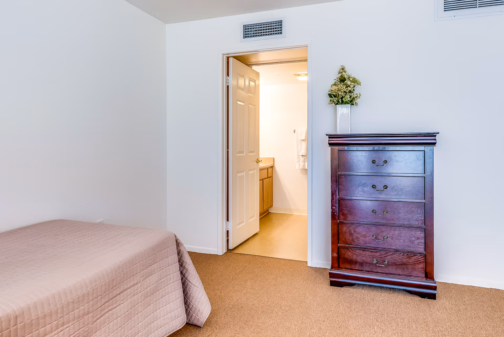 Simple bedroom with a twin bed, a wooden chest of drawers, and an open door leading to a bathroom.