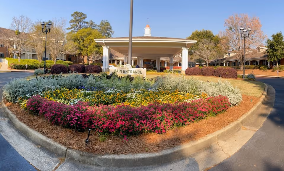 Circular landscaped driveway with colorful flowerbeds leading to a covered main entrance canopy of the building.