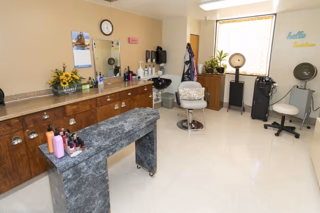 Small salon-style room with a styling chair, shampoo sink, drying stations, cabinets of hair products and a manicure table.