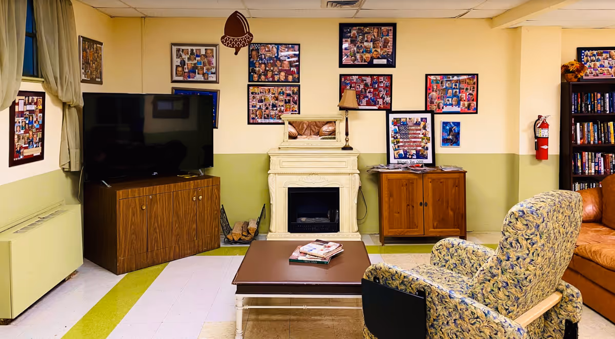 Cozy communal living room with a TV, fireplace, coffee table, armchairs, bookshelf and photo collages on the walls.