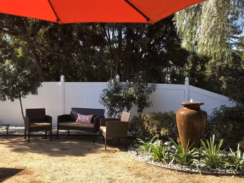 Outdoor seating area with chairs, a red umbrella, white fence, and a fountain.