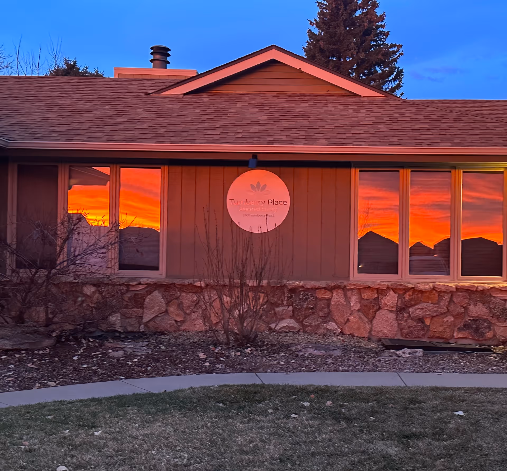 Front exterior of a single-story assisted living building with a circular "Turnberry Place" sign and vivid sunset reflections in the windows.