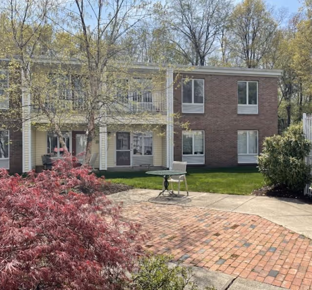 Two-story brick and siding assisted living building with a small patio, table and chair, and landscaped courtyard.