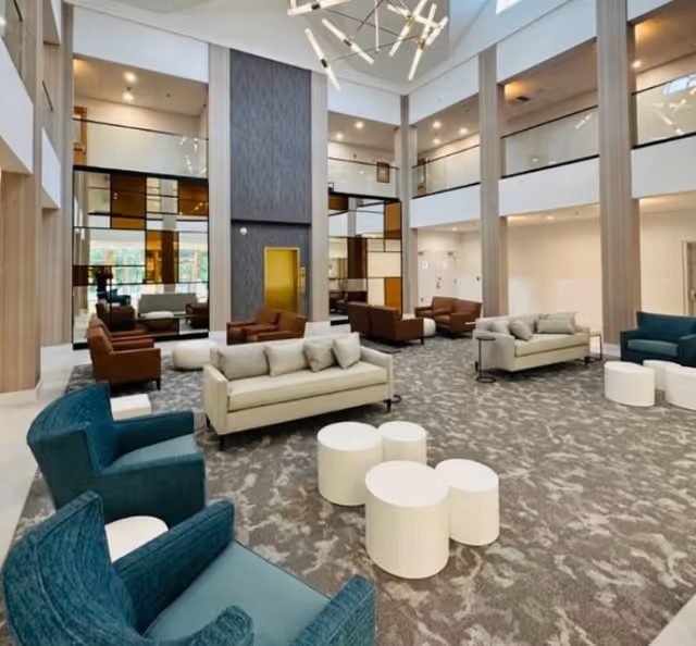 Spacious modern two-story senior living lounge with sofas, armchairs, round white tables, and a chandelier.