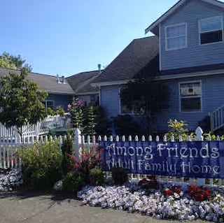 Exterior view of a blue Among Friends Adult Family Home with a flower-filled front yard.