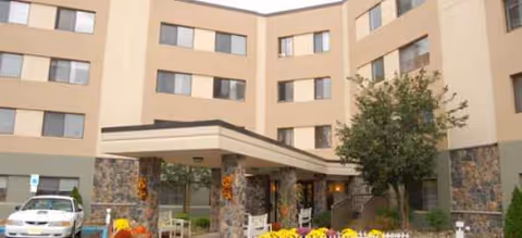 Exterior view of Brookdale Echelon Lake entrance with stone columns and blooming flowers.