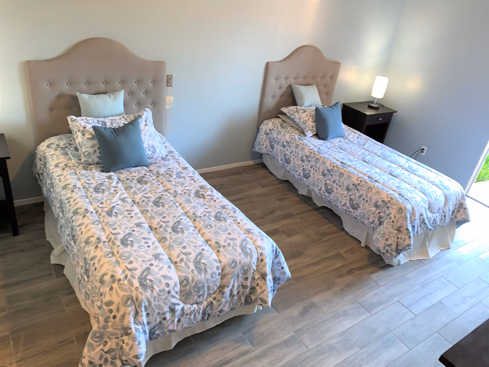Two twin beds with tufted headboards and matching bedding in a light blue bedroom.