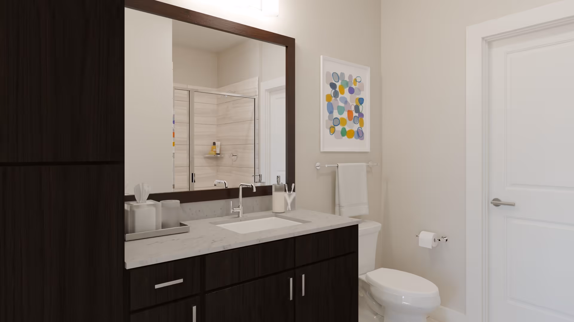 A modern bathroom with dark wood cabinetry, a white countertop with a built-in sink, a large mirror with a dark wood frame, a white toilet, a towel rack with a white towel, a colorful abstract painting on the wall, and a glass-enclosed shower reflected in the mirror.