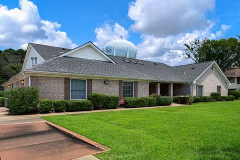 Single story brick assisted living facility with manicured lawn, hedges, and a walkway along the front.