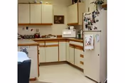 Small L-shaped kitchen with cream cabinets, laminate countertops, a refrigerator covered in photos and a microwave on the counter.