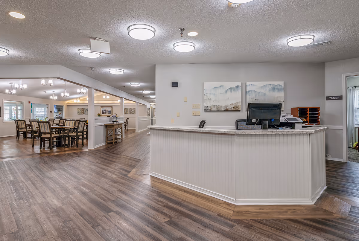 Bright interior showing a curved white reception desk with a computer and an adjacent dining area with tables and chairs.