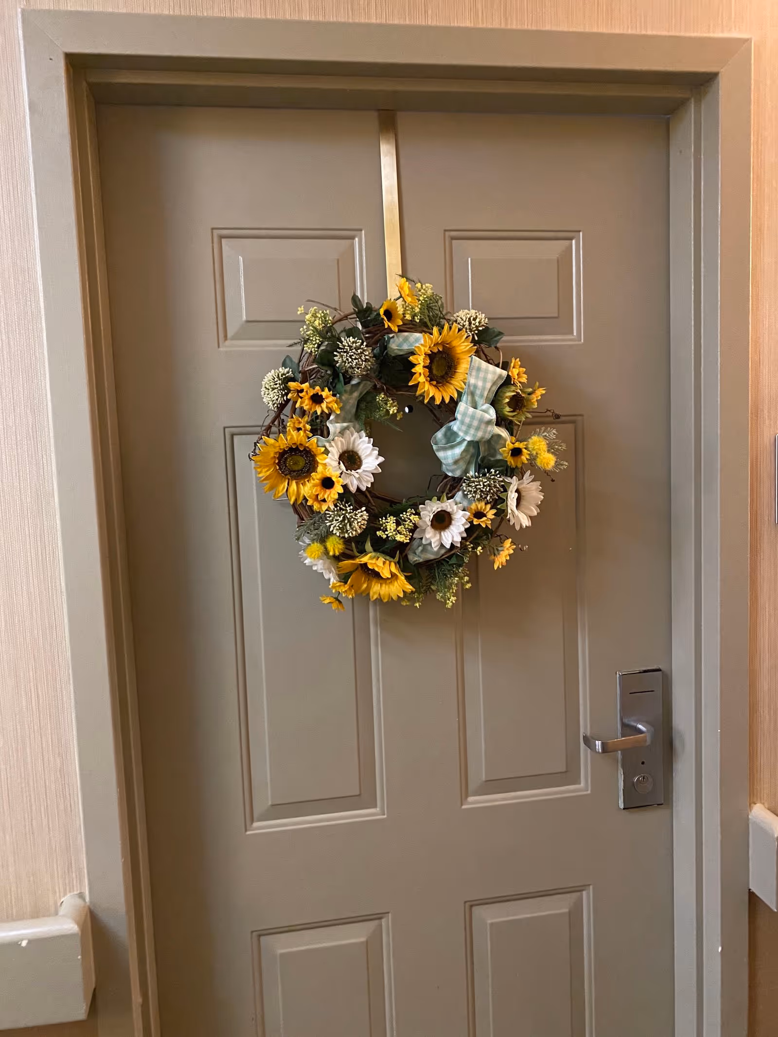 Gray interior door decorated with a sunflower and daisy wreath hanging on a gold ribbon in a hallway.