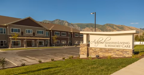 Exterior of Ashford Assisted Living & Memory Care building with sign and mountainous backdrop.