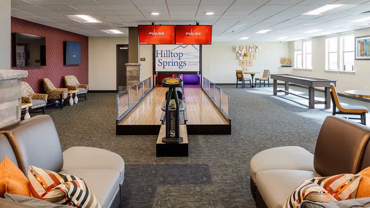 Recreation room at Hilltop Springs Senior Living with a short bowling lane, seating areas, and game tables.