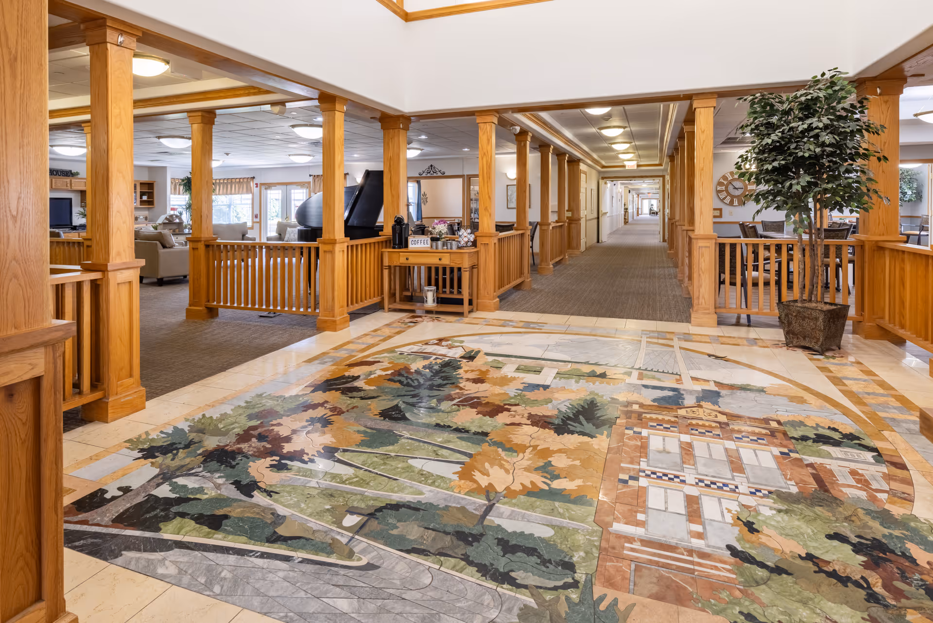 Lobby and common area with wooden columns, a decorative floor mural, seating areas, and a long hallway.