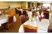 Dining room with rows of tables set with white tablecloths, napkins and floral centerpieces and wooden chairs.