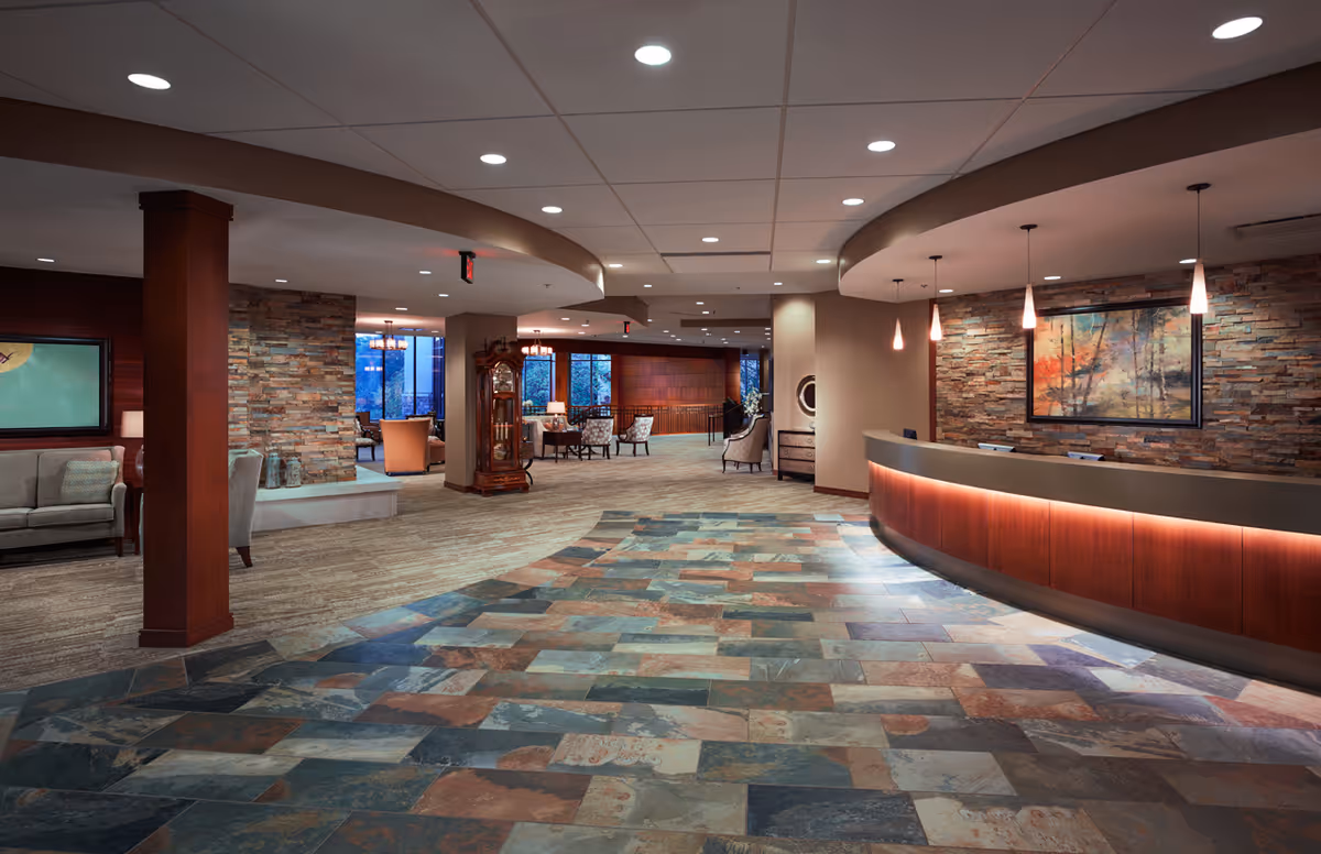 Spacious lobby with a curved reception desk, stone accent walls, seating areas, and patterned tile floor.