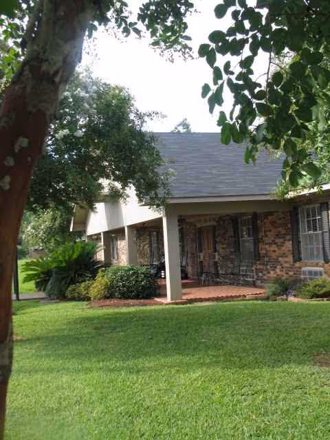 Brick senior living center exterior with covered entrance, green lawn, trees, and shrubs.