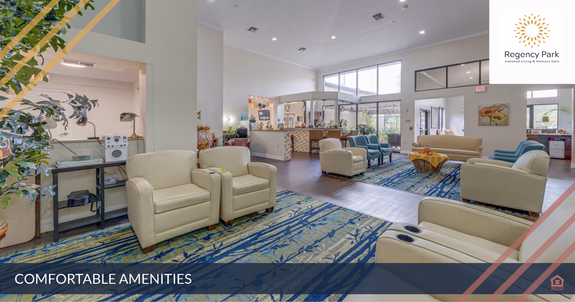 A spacious and well-lit common area in Regency Park Assisted Living & Memory Care featuring multiple comfortable armchairs and sofas arranged around a central coffee table on a patterned carpet. Large windows allow natural light to fill the room, and there are plants and decorative elements enhancing the welcoming atmosphere.
