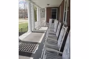 Covered front porch with a row of white wooden rocking chairs, columns, and a brick exterior.