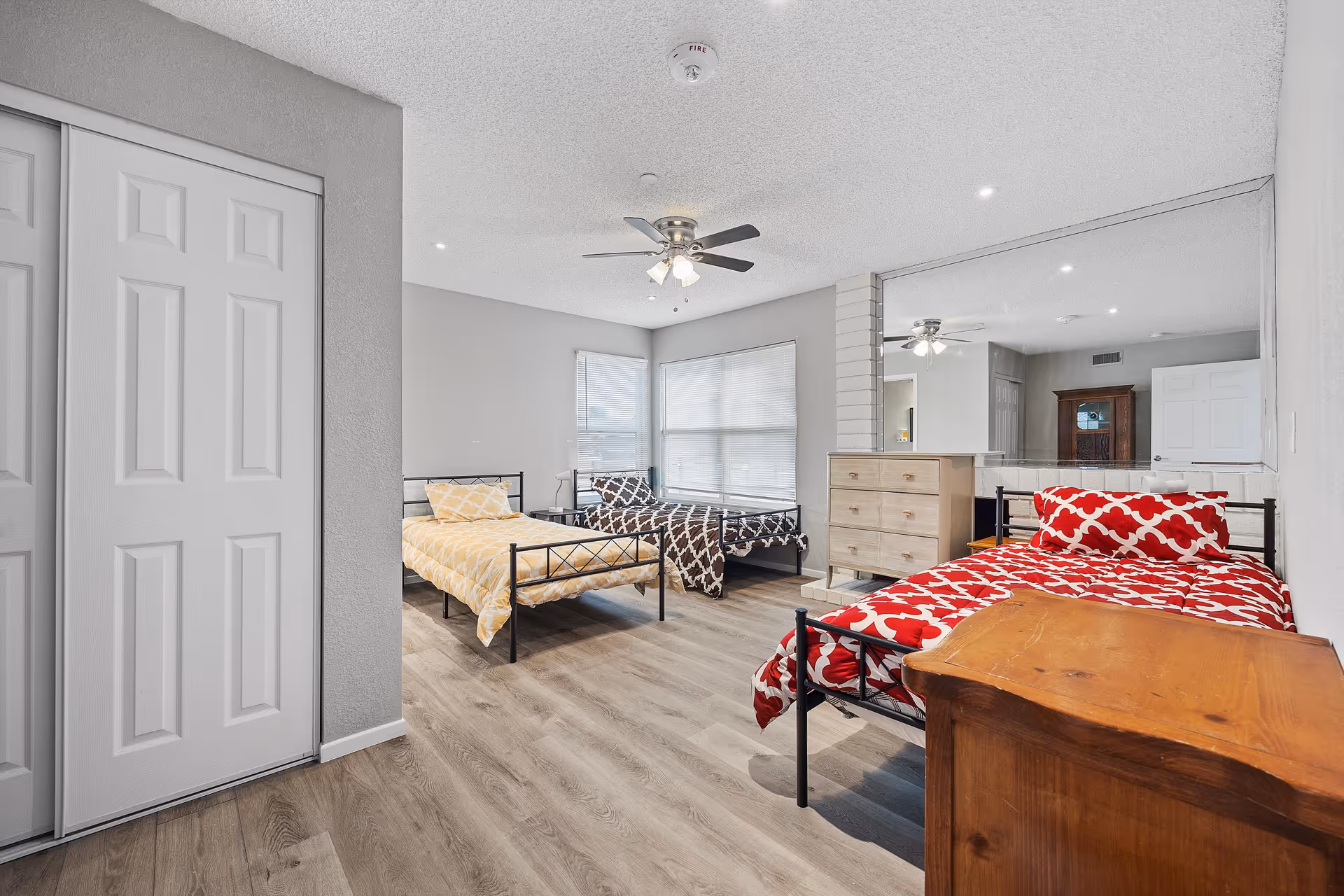 Large shared bedroom with three single beds, a dresser, ceiling fan, and wood-look flooring.