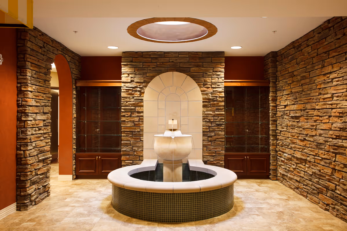 An indoor decorative fountain centered in a stone-walled lobby with tiled floor and built-in display cabinets.