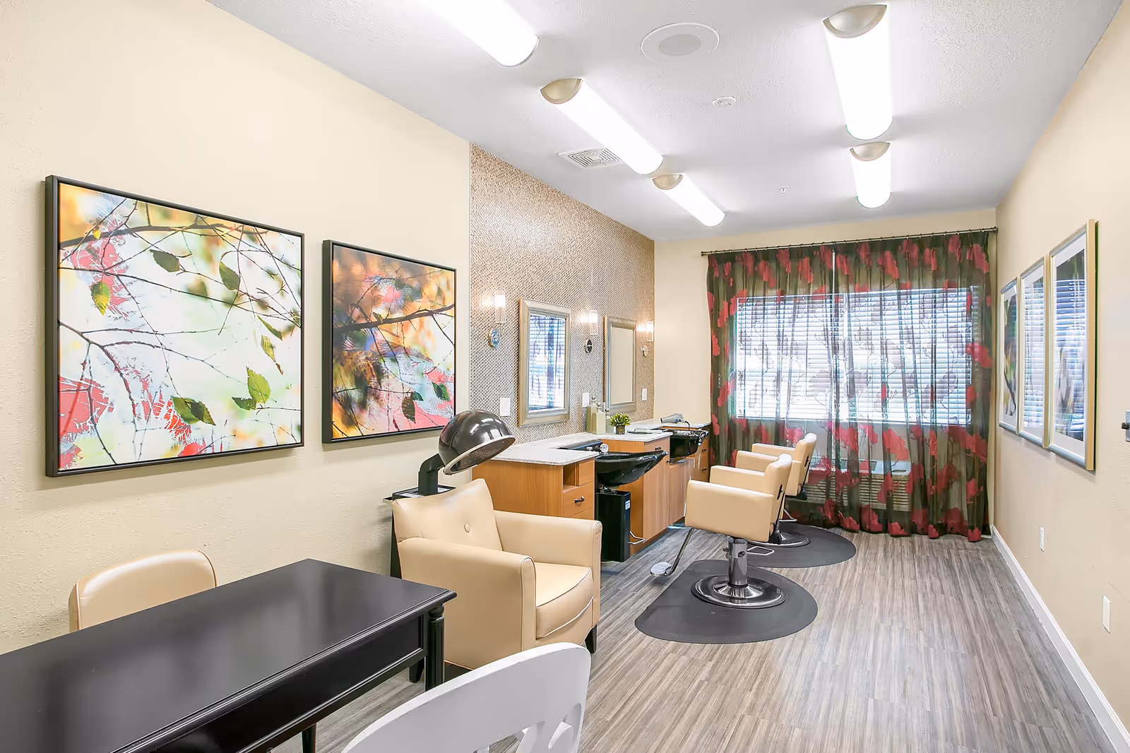 Bright salon room with styling chairs, shampoo sinks, colorful wall art, and a large window with floral curtains.