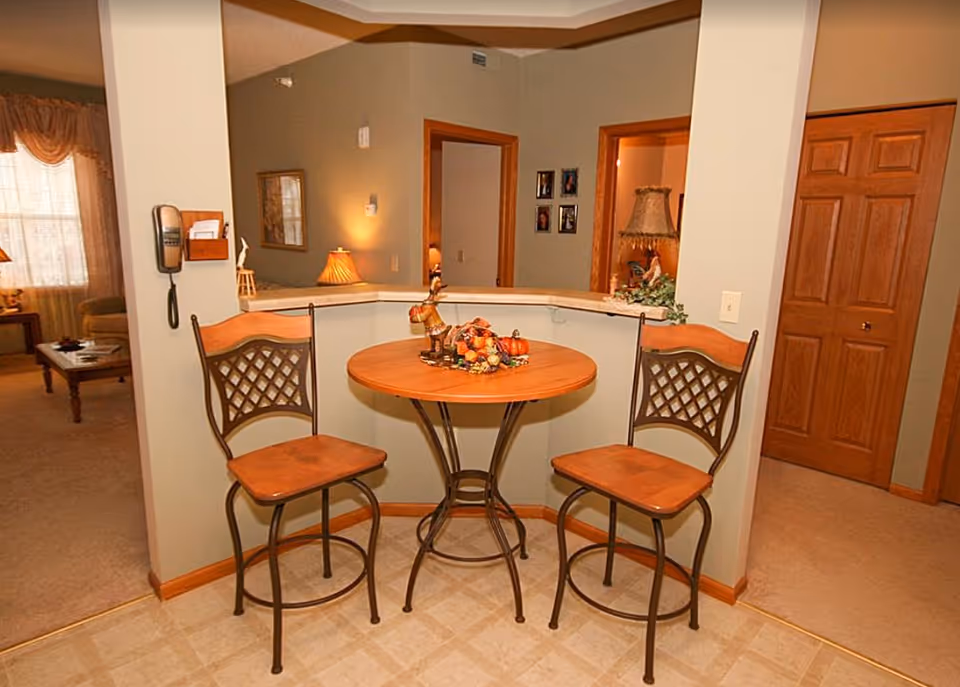 Round wooden bistro table with two high chairs and an autumn centerpiece in an open-plan living area.