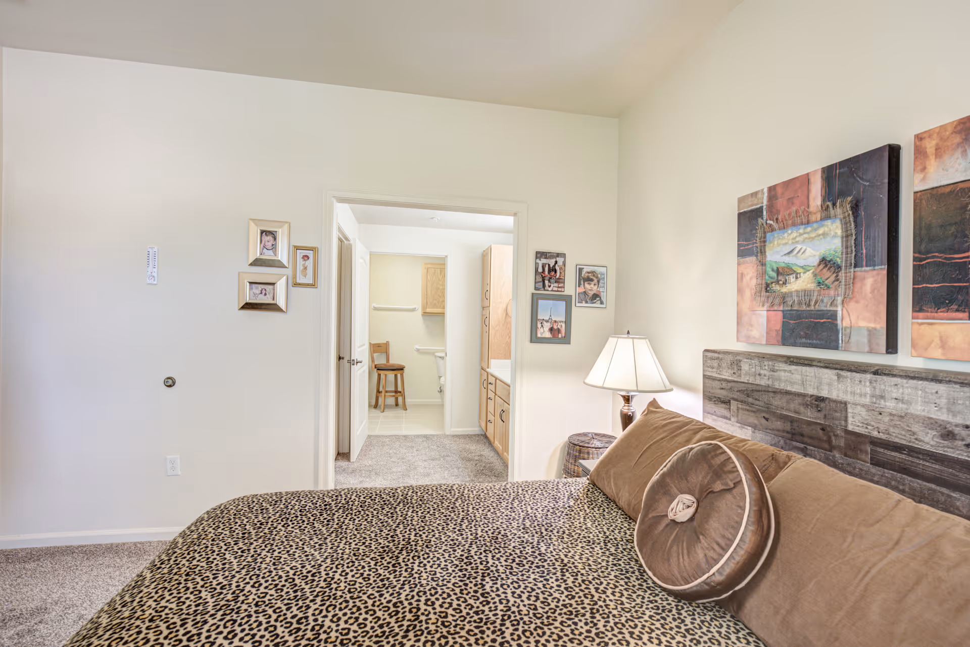 Bedroom with a leopard-print bedspread, rustic headboard, bedside lamp, and an open doorway leading to a bathroom.