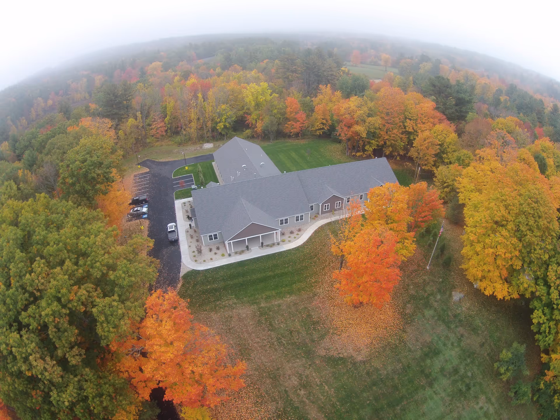Aerial view of a single-story assisted living building with a parking lot, lawns, and colorful fall trees surrounding it.