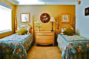 Two twin beds with floral bedding flank a central dresser and lamp in a sunny bedroom