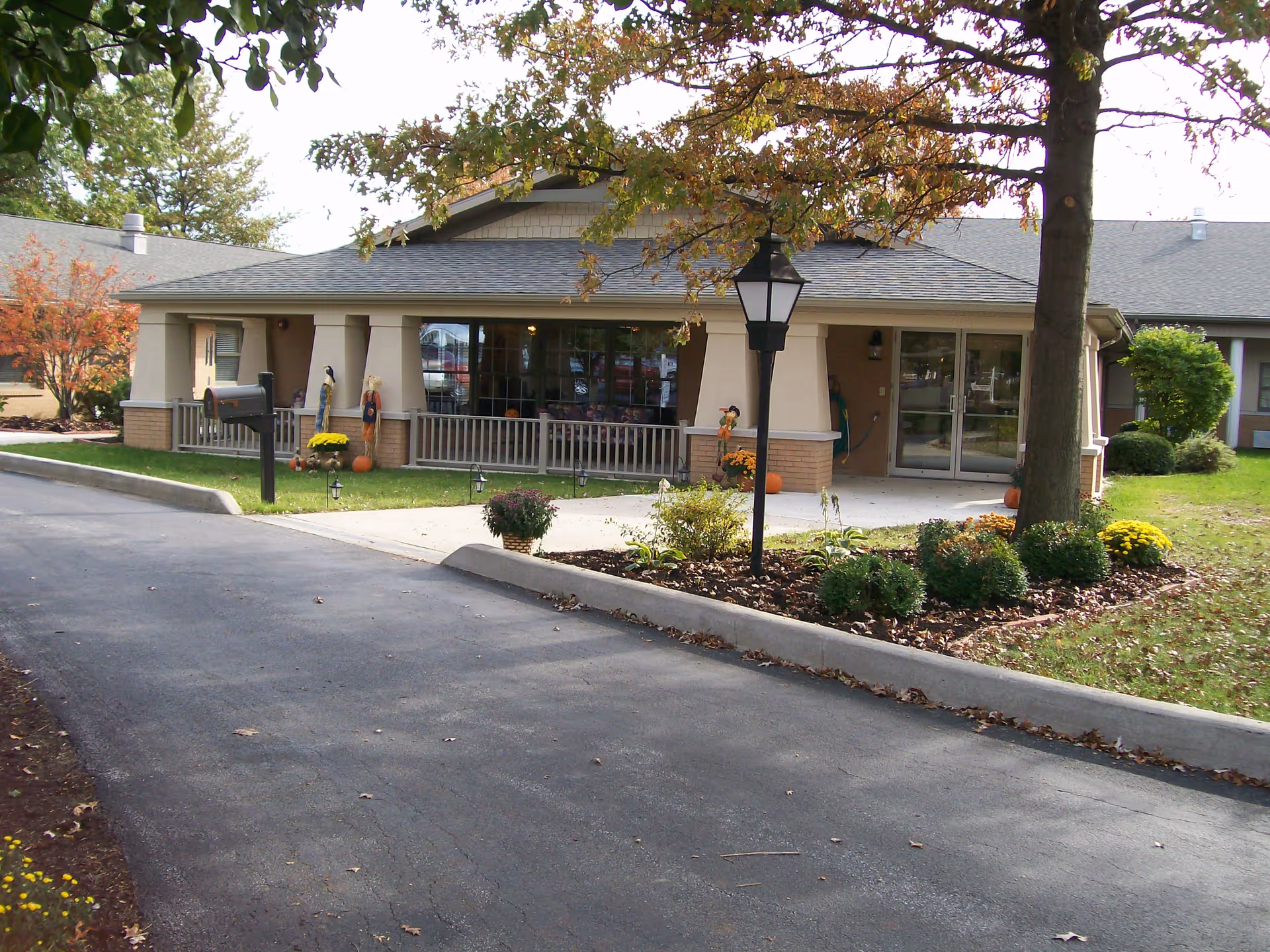 Single-story building entrance with a covered porch, lamp post, landscaping and a paved driveway.
