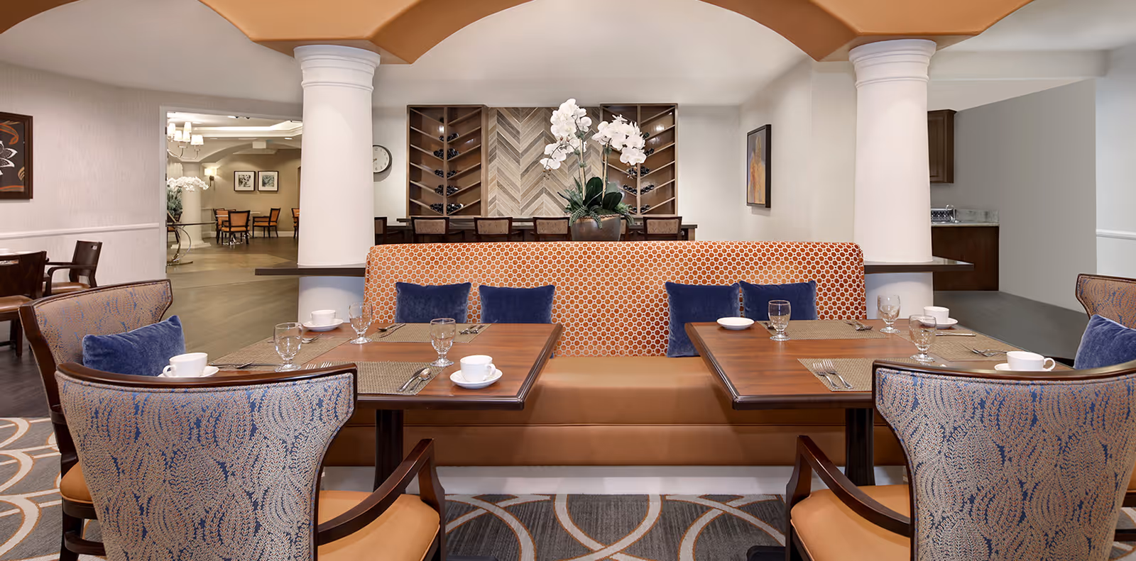 Dining room with booth seating, tables set with cups and glasses, upholstered chairs and decorative columns.