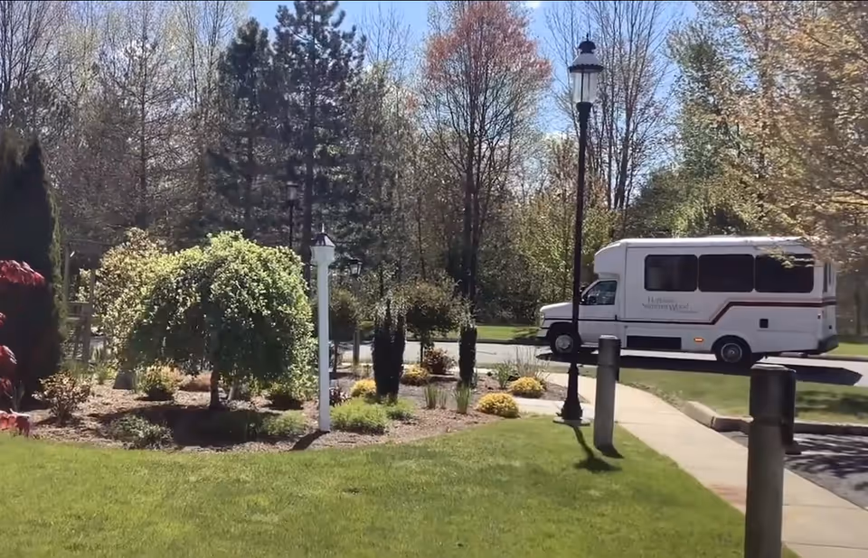 Landscaped front lawn and garden with lamp posts and a white shuttle van parked on the driveway.