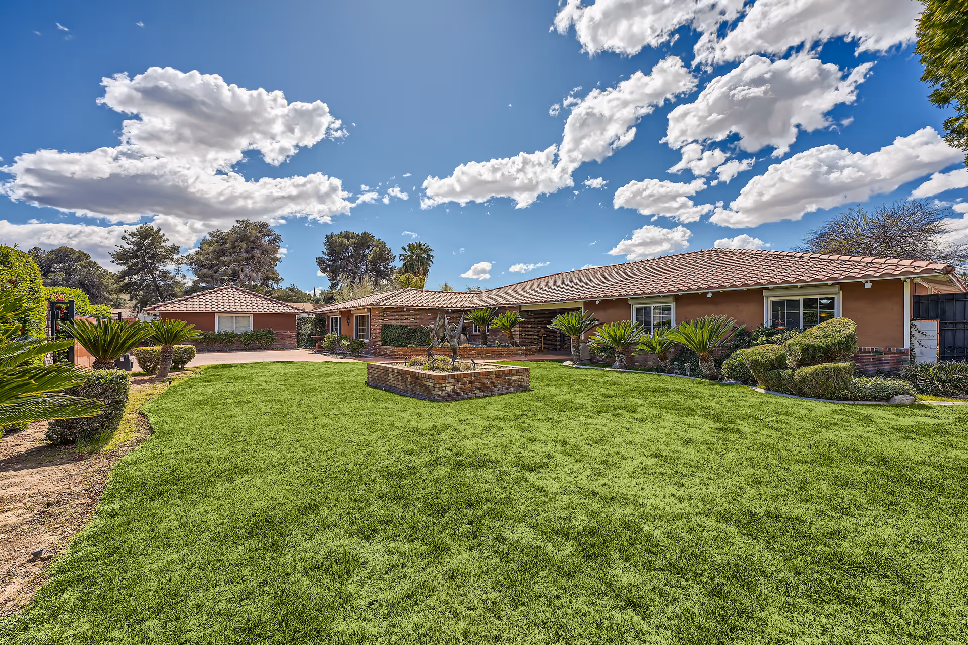 Single-story building with a tiled roof, manicured lawn and a central brick planter under a blue sky.
