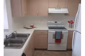 Small galley kitchen with light wood cabinets, a double sink, white refrigerator and stove with towels.
