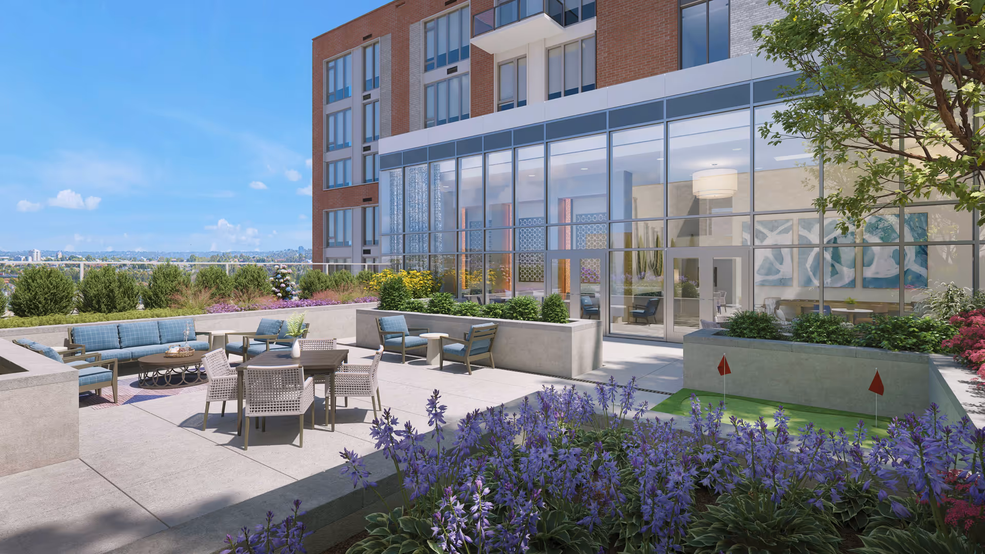 Rooftop courtyard with lounge seating, a dining table, planters and purple flowers beside a glass-walled building and a small putting green.