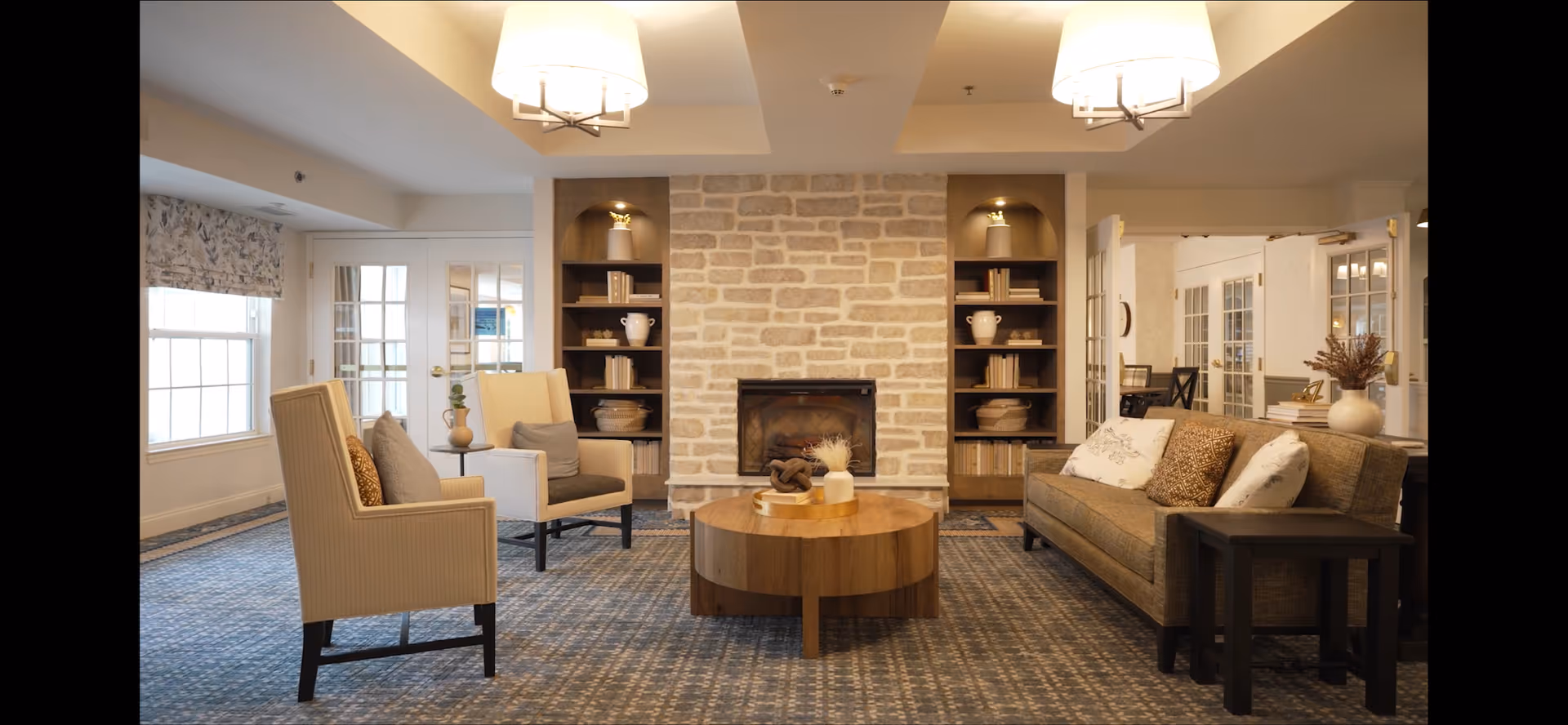 Comfortable communal living room with seating arranged around a central wooden coffee table and a stone fireplace.