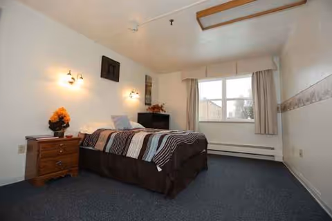 Small, simply furnished bedroom with a bed, nightstand, and window.
