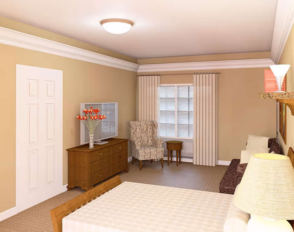 A cozy living room with beige walls and carpet. The room features a wooden dresser with a vase of red flowers and a flat-screen TV on top, a patterned armchair next to a small round wooden table by a window with beige curtains, and a brown sofa with white cushions. A table with a light-colored quilted cover and a lamp with a beige shade are also visible.