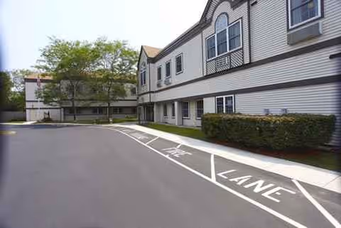Exterior view of Village House Nursing & Rehabilitation Center with driveway and trees.