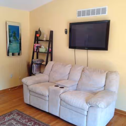 Yellow walls create a living room with a beige sofa, mounted TV, and shelving.