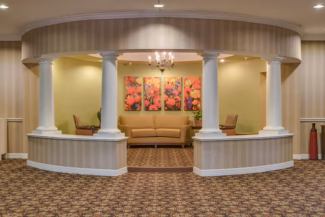 A seating alcove with a sofa and chairs framed by white columns and floral artwork on the back wall.