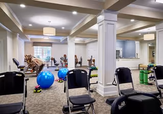 Spacious, well-lit exercise room with chairs, stability balls, dumbbells, exercise machines, and mirrors separated by decorative columns.