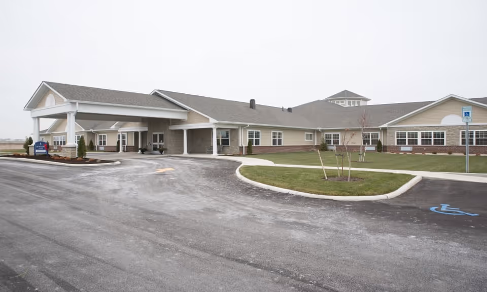Single-story senior living facility building with a covered entrance, driveway, landscaped islands, and a handicap parking space.
